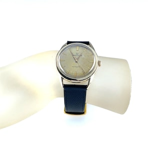 May include: Silver wristwatch with a light-coloured face and black leather strap. The watch has a round face with a silver bezel and a dark blue leather strap. The word "AUTOMATIC" is printed on the watch face.