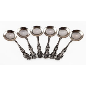 Puede incluir: Juego de seis cucharaditas de plata con mangos ornamentados. Las cucharas tienen un cuenco redondeado y un diseño floral decorativo en el mango.