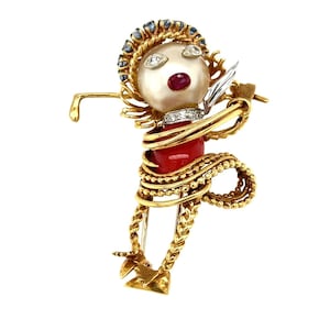 May include: A gold brooch in the form of a figure, with a pearl head, diamond and ruby details, and a red coral body. The figure is wrapped in gold wire, and the headpiece is decorated with blue gemstones.