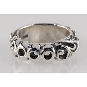 Peut inclure: Une bague en argent avec un design orné. La bague présente une série de découpes circulaires et de motifs tourbillonnants. Le métal a une surface polie et réfléchissante. La bague est probablement en argent sterling ou dans un matériau similaire.