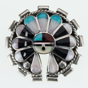 May include: A silver ring with a turquoise and mother-of-pearl inlay in the shape of a stylized flower. The ring is set with a black and white stone in the center.