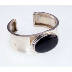Puede incluir: Un brazalete de plata con una gran piedra ovalada negra engastada en un bisel de plata.