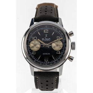 May include: A vintage Le Jour chronograph watch with a black dial, gold sub-dials, and a stainless steel case. The watch features a black leather strap with perforations. The dial displays the text "LE JOUR 17 JEWELS" and "INCABLOC".
