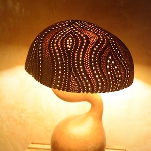 May include: A gourd lamp with a carved, patterned shade. The shade is lit from within, casting a warm glow. The base of the lamp is a natural gourd with a curved, organic shape.