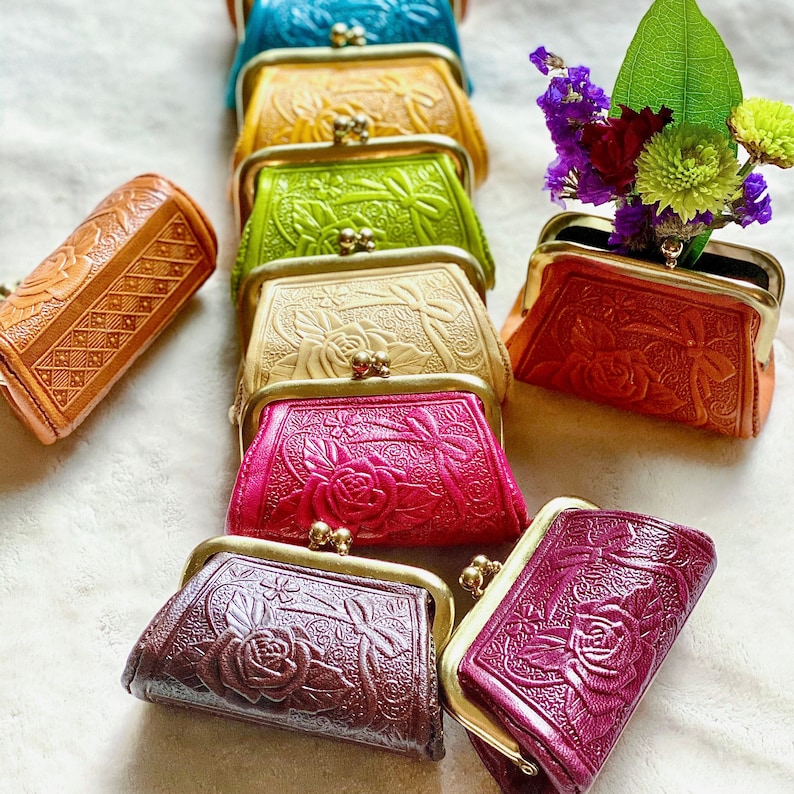 Peut inclure: Une collection de petits porte-monnaie rectangulaires de diff&eacute;rentes couleurs, dont bleu, jaune, vert lime, beige, rose, brun fonc&eacute; et bordeaux. Chaque porte-monnaie pr&eacute;sente un motif gaufr&eacute; de roses et de rubans avec un fermoir &agrave; clip dor&eacute;.