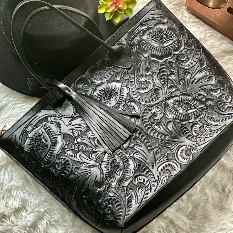 Black Handmade tooled leather tote bag for women with floral embossing, large zippered compartment, and boho-chic style. This personalized leather tote purse is perfect as a floral work bag or everyday handbag.