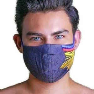 May include: A blue face mask with a yellow sun and red and blue stripes on the side. The mask is made of fabric and has a blue elastic band.