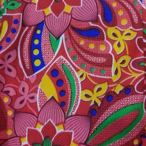 May include: A red fabric with a floral pattern. The flowers are pink, red, yellow, green, and blue. The fabric has a paisley design.