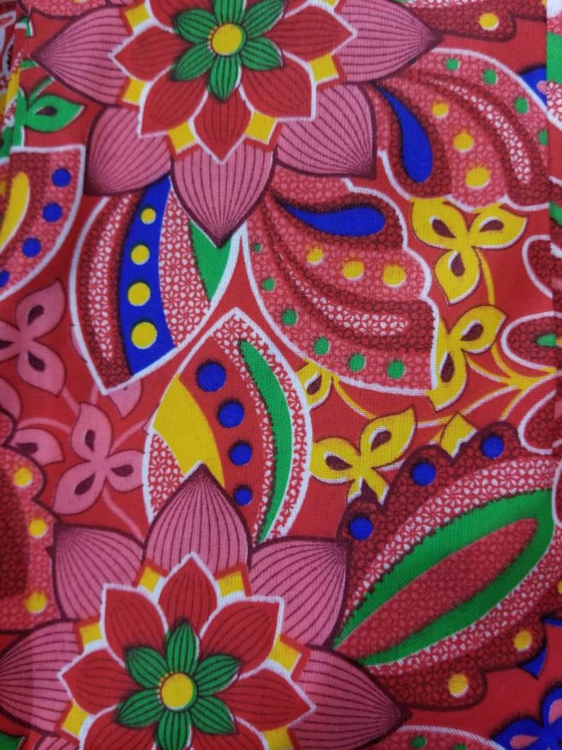 May include: A red fabric with a floral pattern. The flowers are pink, red, yellow, green, and blue. The fabric has a paisley design.