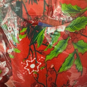May include: Red fabric with a green and white floral pattern. The fabric has a snowflake design and the text "ONS NES" is visible in the top left corner.