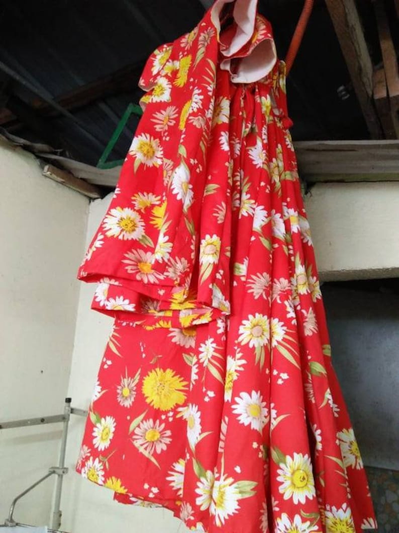 May include: A red dress with a white daisy print. The dress has a gathered waist and a ruffled neckline.