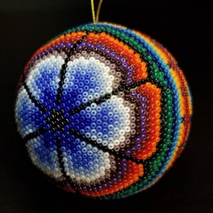 May include: A round, beaded ornament with a basketball design. The ornament features a vibrant colour palette of blue, white, orange, green, and purple beads. A gold string is attached for hanging.