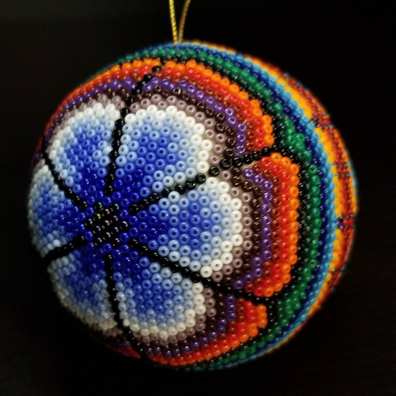 May include: A round, beaded ornament with a basketball design. The ornament features a vibrant colour palette of blue, white, orange, green, and purple beads. A gold string is attached for hanging.