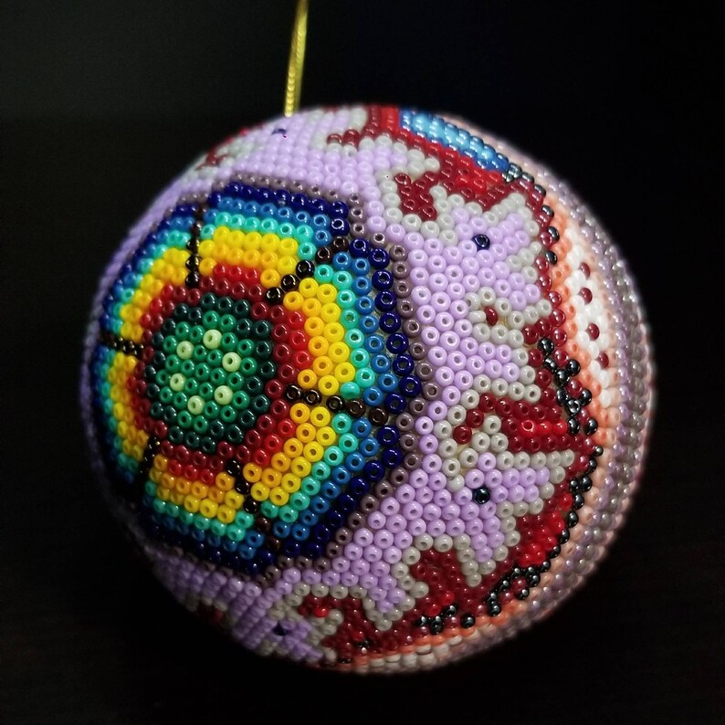 May include: A detailed, beaded sphere ornament with a complex geometric design. The ornament features a central rainbow pattern, surrounded by lavender, red, and white beaded sections. A gold string is attached for hanging. Suitable for festive decorations.