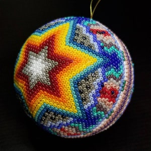 May include: A beaded Christmas bauble with a star design. The bauble features a star in the centre with a white background, surrounded by red, yellow, and blue beads. The rest of the bauble is covered in a variety of colourful beads.