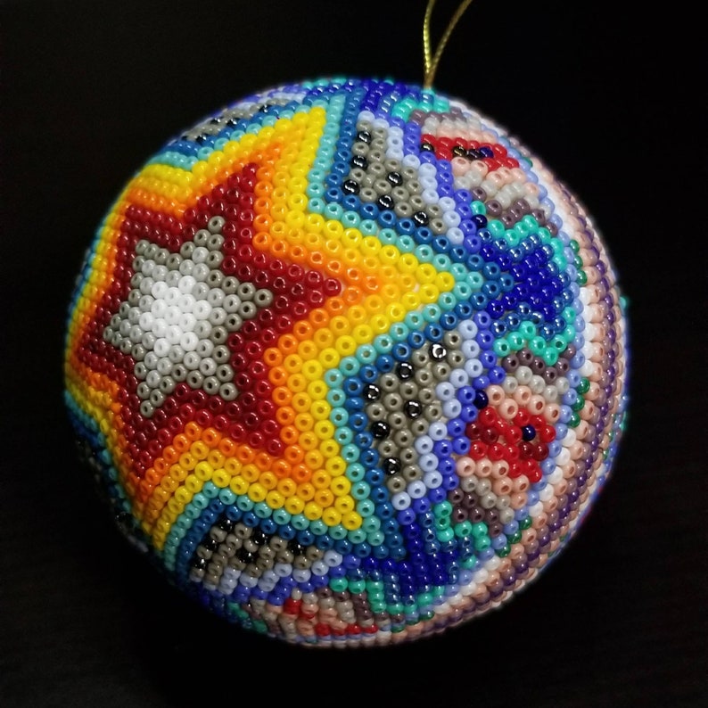 May include: A beaded Christmas bauble with a star design. The bauble features a star in the centre with a white background, surrounded by red, yellow, and blue beads. The rest of the bauble is covered in a variety of colourful beads.