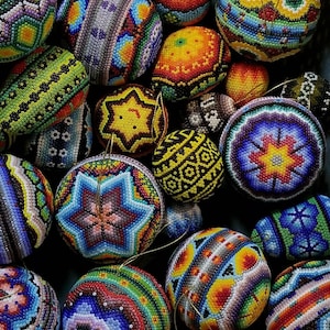May include: A selection of vibrantly coloured, beaded ornaments. The decorations display intricate patterns in shades of blue, yellow, red, and green. Some have star and geometric designs. These handmade ornaments showcase a vibrant display of craftsmanship.