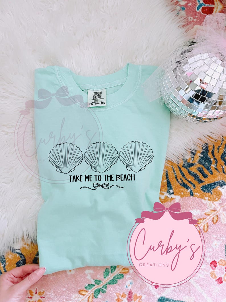 May include: A light blue t-shirt with a graphic of three seashells and the text "Take Me To The Beach".