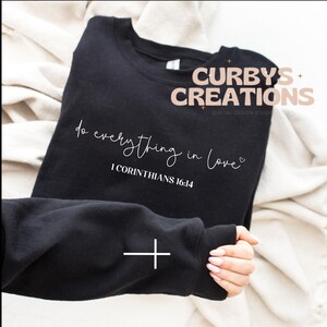 May include: Black sweatshirt with white text that reads "do everything in love" and "1 Corinthians 16:14". The text is in a cursive font. The sweatshirt is on a white surface.