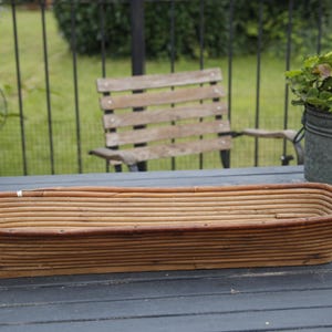 Könnte beinhalten: Ein langer, rechteckiger, geflochtener Korb aus Weide mit natürlicher brauner Farbe. Der Korb ist leer und steht auf einer dunklen Holzoberfläche.