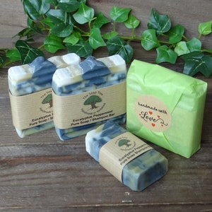 May include: Several bars of handmade soap are displayed, some wrapped in brown paper and others in green tissue. The soap bars have a marbled appearance with blue and white swirls. One bar is wrapped with a label that reads "Eucalyptus Peppermint Pure Soap / Shampoo Bar."