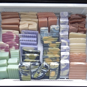 May include: A white plastic container with a wire mesh insert filled with handmade bars of soap in various colours and patterns. The soap bars are arranged in rows and columns.