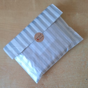 May include: A white and grey striped paper bag with a brown circle sticker that says "handmade with love" in black text with a red heart.