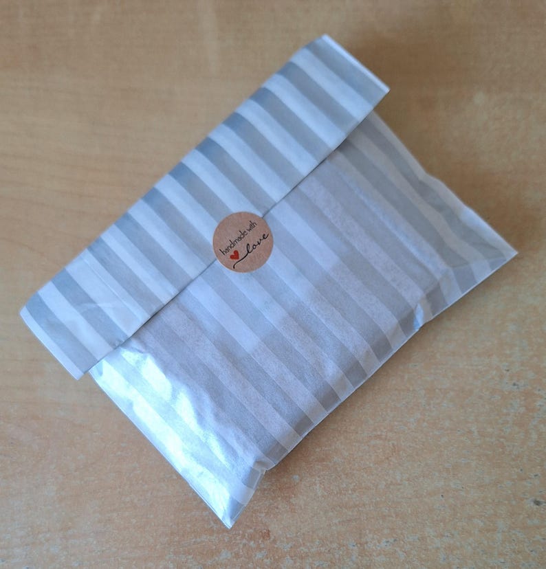 May include: A white and grey striped paper bag with a brown circle sticker that says "handmade with love" in black text with a red heart.