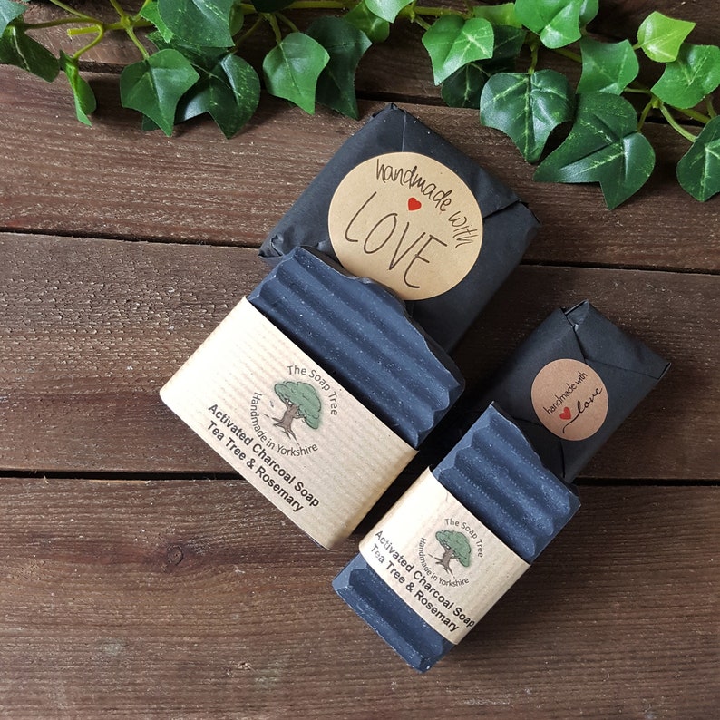 Puede incluir: Dos pastillas de jab&oacute;n de carb&oacute;n activado gris oscuro con &aacute;rbol de t&eacute; y romero, envueltas en papel negro con una etiqueta color canela que dice The Soap Tree, Handmade in Yorkshire, y una pegatina redonda handmade with LOVE con un peque&ntilde;o coraz&oacute;n rojo.