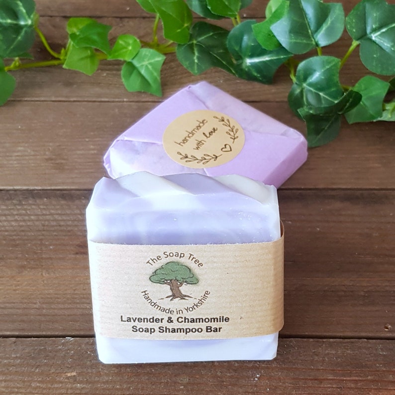 May include: A lavender and chamomile soap shampoo bar from The Soap Tree, handmade in Yorkshire. The bar is wrapped in a brown paper band with the brand's logo and product details. A second wrapped bar is in the background, with a sticker that says "handmade with love."