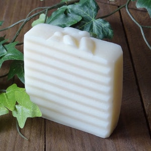 May include: A white bar of soap with a ribbed texture and a raised design on the top. The soap is sitting on a wooden surface.