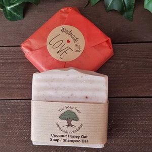 May include: A bar of Coconut Honey Oat Soap / Shampoo Bar from The Soap Tree, handmade in Yorkshire, wrapped in a brown paper band. The soap is next to a red paper-wrapped package with a "handmade with LOVE" sticker.