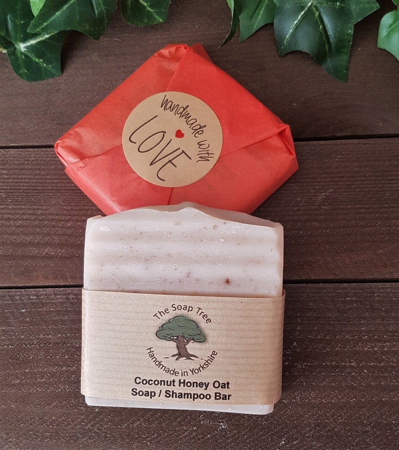 May include: A bar of Coconut Honey Oat Soap / Shampoo Bar from The Soap Tree, handmade in Yorkshire, wrapped in a brown paper band. The soap is next to a red paper-wrapped package with a "handmade with LOVE" sticker.
