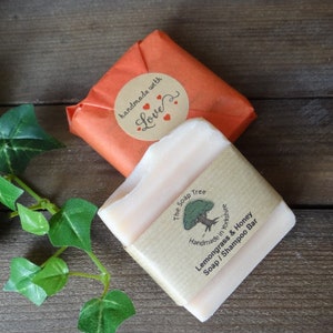May include: A light-colored Lemongrass & Honey Soap/Shampoo Bar from The Soap Tree, wrapped in brown paper with a label. The bar is partially visible, with a second bar wrapped in orange paper and a "handmade with love" sticker.