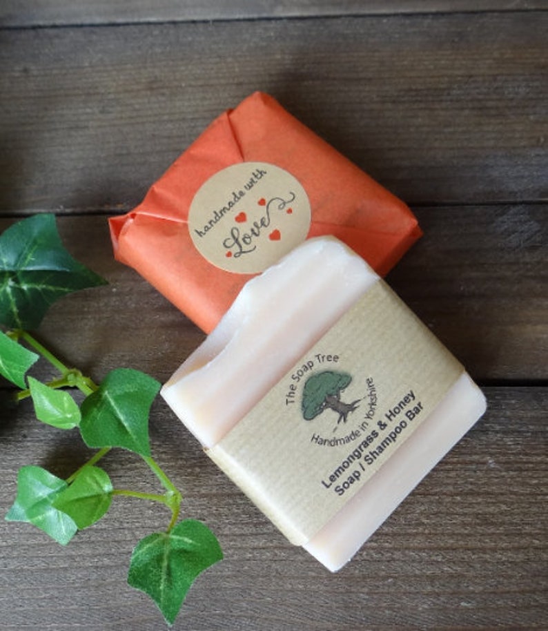 May include: A light-colored Lemongrass & Honey Soap/Shampoo Bar from The Soap Tree, wrapped in brown paper with a label. The bar is partially visible, with a second bar wrapped in orange paper and a "handmade with love" sticker.