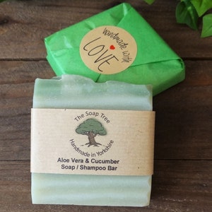May include: A green bar of soap with a brown label that reads "The Soap Tree Handmade in Yorkshire Aloe Vera & Cucumber Soap / Shampoo Bar". The soap is wrapped in green tissue paper with a brown circle sticker that reads "Handmade with Love" with a red heart.