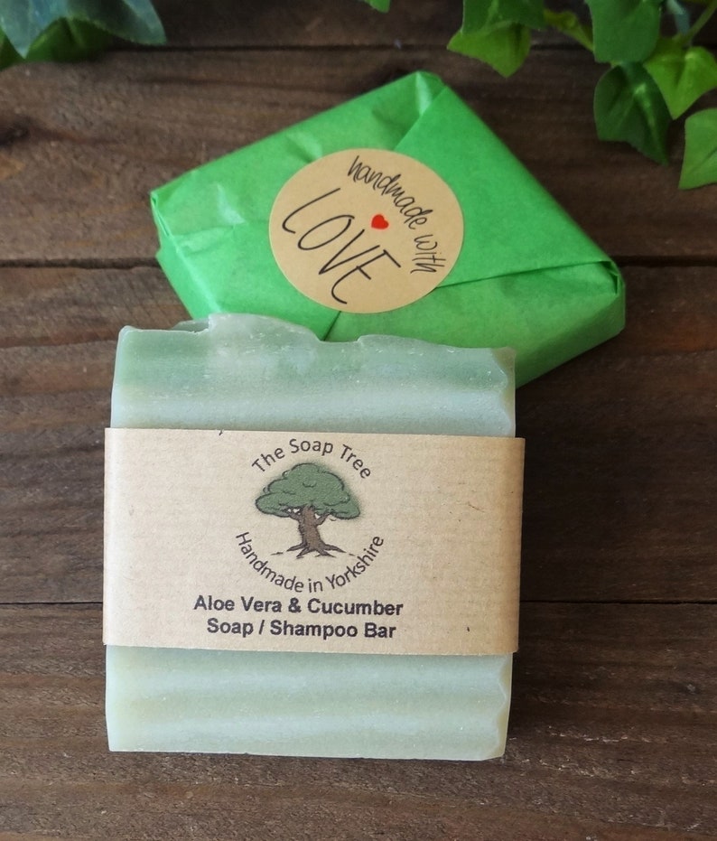 May include: A green bar of soap with a brown label that reads "The Soap Tree Handmade in Yorkshire Aloe Vera & Cucumber Soap / Shampoo Bar". The soap is wrapped in green tissue paper with a brown circle sticker that reads "Handmade with Love" with a red heart.