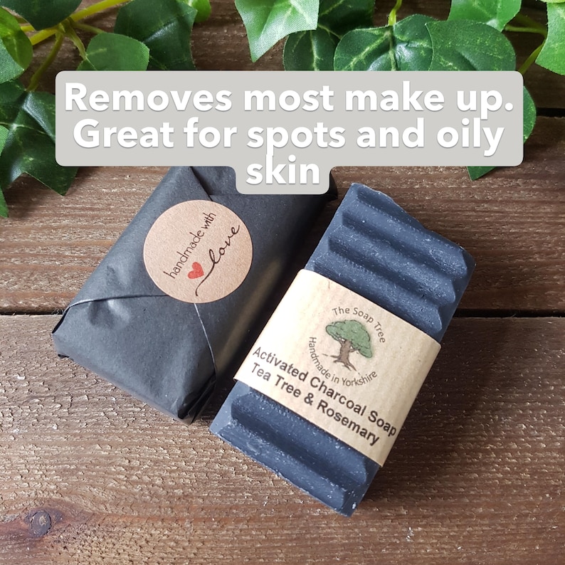 Puede incluir: Dos barras de jab&oacute;n de carb&oacute;n activado gris oscuro. Una barra est&aacute; envuelta en papel negro con una pegatina redonda que dice 'handmade with love'. La otra tiene una banda de papel color canela etiquetada 'The Soap Tree Activated Charcoal Soap Tea Tree & Rosemary'. El texto dice: 'Removes most make up. Great for spots and oily skin'.