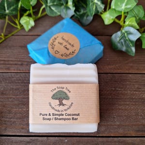 May include: A white Pure & Simple Coconut Soap / Shampoo Bar with a brown paper label from The Soap Tree, handmade in Yorkshire. A blue wrapped package with a "handmade with love" sticker is in the background. Green leaves are in the background.
