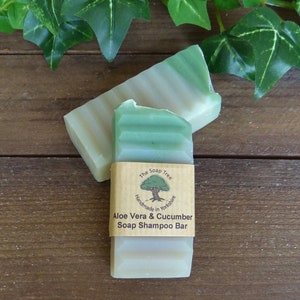 May include: A green and white bar of soap shampoo with a brown label that reads "The Soap Tree Handmade in Yorkshire Aloe Vera & Cucumber Soap Shampoo Bar".