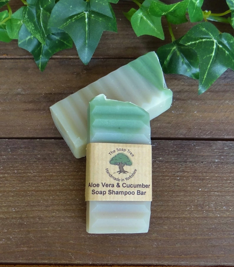 May include: A green and white bar of soap shampoo with a brown label that reads "The Soap Tree Handmade in Yorkshire Aloe Vera & Cucumber Soap Shampoo Bar".