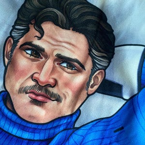 May include: A fabric print featuring a stylized illustration of a person with dark hair, a mustache, and brown eyes. The figure wears a bright blue turtleneck sweater and has one arm raised behind their head, set against a white background.