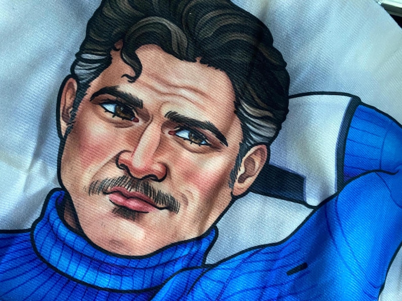 May include: A fabric print featuring a stylized illustration of a person with dark hair, a mustache, and brown eyes. The figure wears a bright blue turtleneck sweater and has one arm raised behind their head, set against a white background.