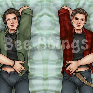 May include: Two men lying on a plaid bedspread. The man on the left is wearing a green shirt, black pants, and headphones. The man on the right is wearing a red plaid shirt, black pants, and a knife.