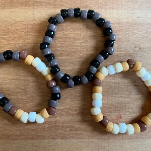 May include: Three beaded bracelets, one black and brown, one brown and white, and one white and tan.
