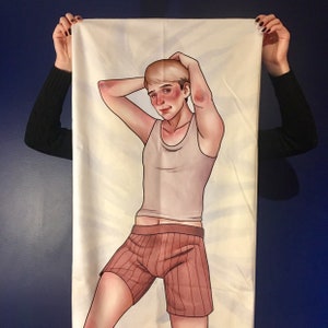 May include: A rectangular fabric body pillowcase featuring a printed illustration of a person with short blonde hair, wearing a light-colored tank top and brown striped boxer shorts, with both arms raised behind their head in a relaxed pose.