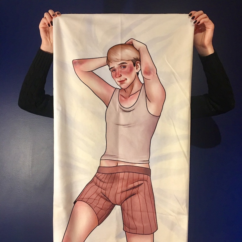 May include: A rectangular fabric body pillowcase featuring a printed illustration of a person with short blonde hair, wearing a light-colored tank top and brown striped boxer shorts, with both arms raised behind their head in a relaxed pose.