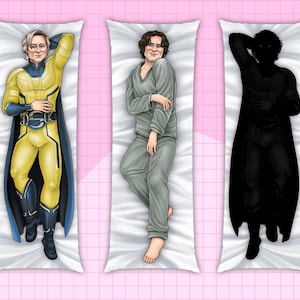 May include: Three body pillow covers featuring illustrations of figures in various poses. One is a superhero in a yellow and blue costume, another in gray pajamas, and the third is a black silhouette. The pillows are rectangular and rest on a pink grid background.