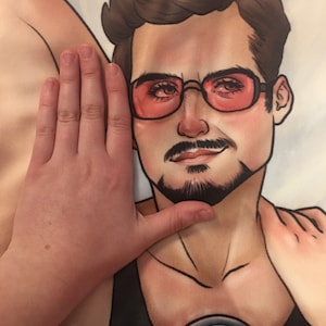 May include: A black and white illustration of a man with brown hair wearing a black tank top with a silver circle on the front. The man is wearing red sunglasses and has a mustache and beard.