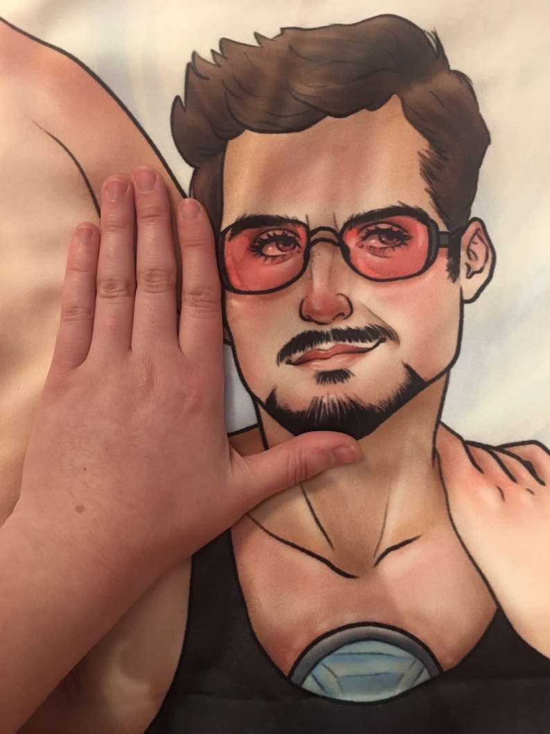 May include: A black and white illustration of a man with brown hair wearing a black tank top with a silver circle on the front. The man is wearing red sunglasses and has a mustache and beard.
